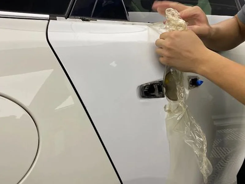 Cheap paint protection film being pulled off the door of a white car, yellowed and stretched out of shape