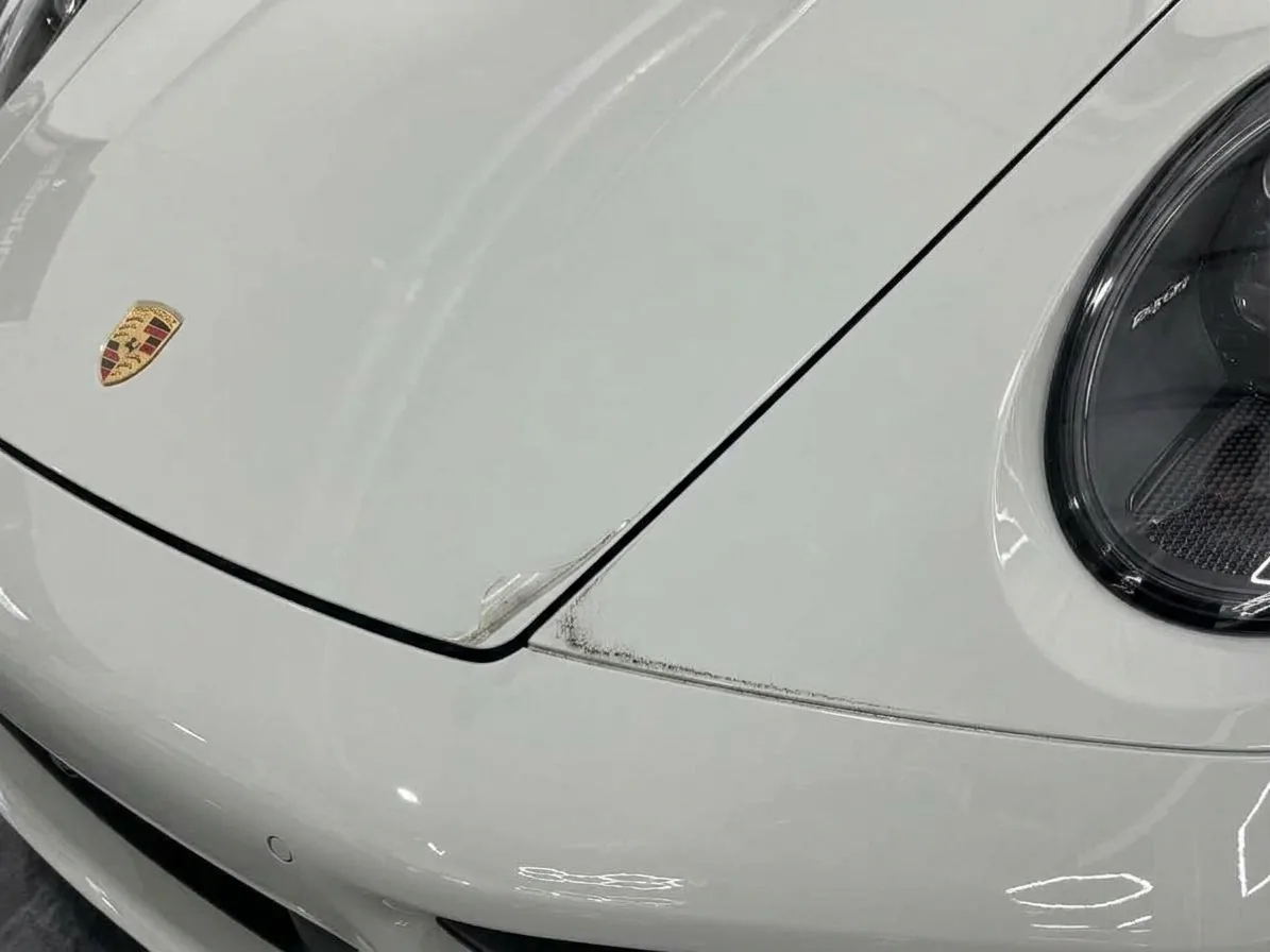 Chalk white Porsche 911 hood edge with film stopping short of the edge, a visible seam and a lifting corner collecting dirt